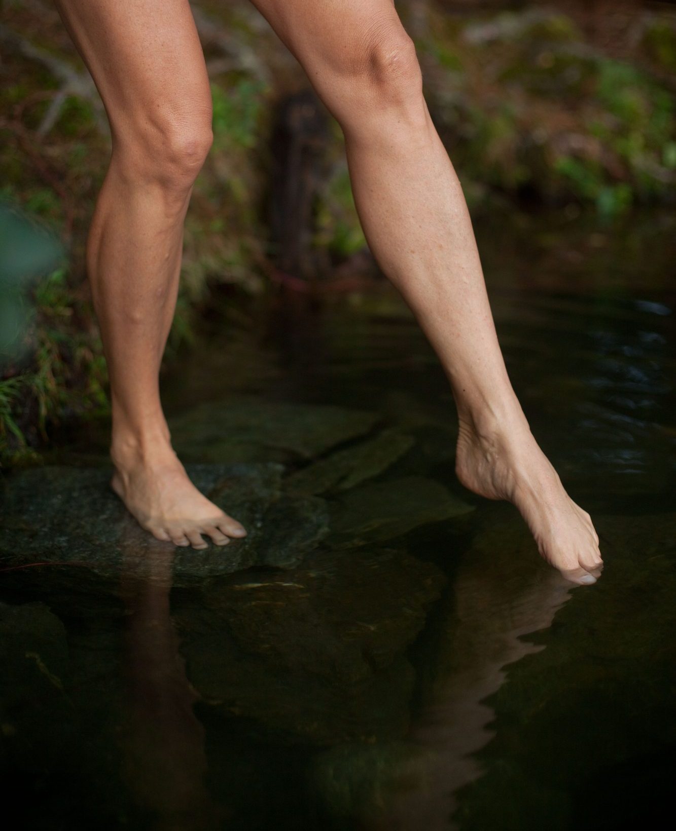 Bloße Beine, eine Zehenspitze tastet ins Wasser
