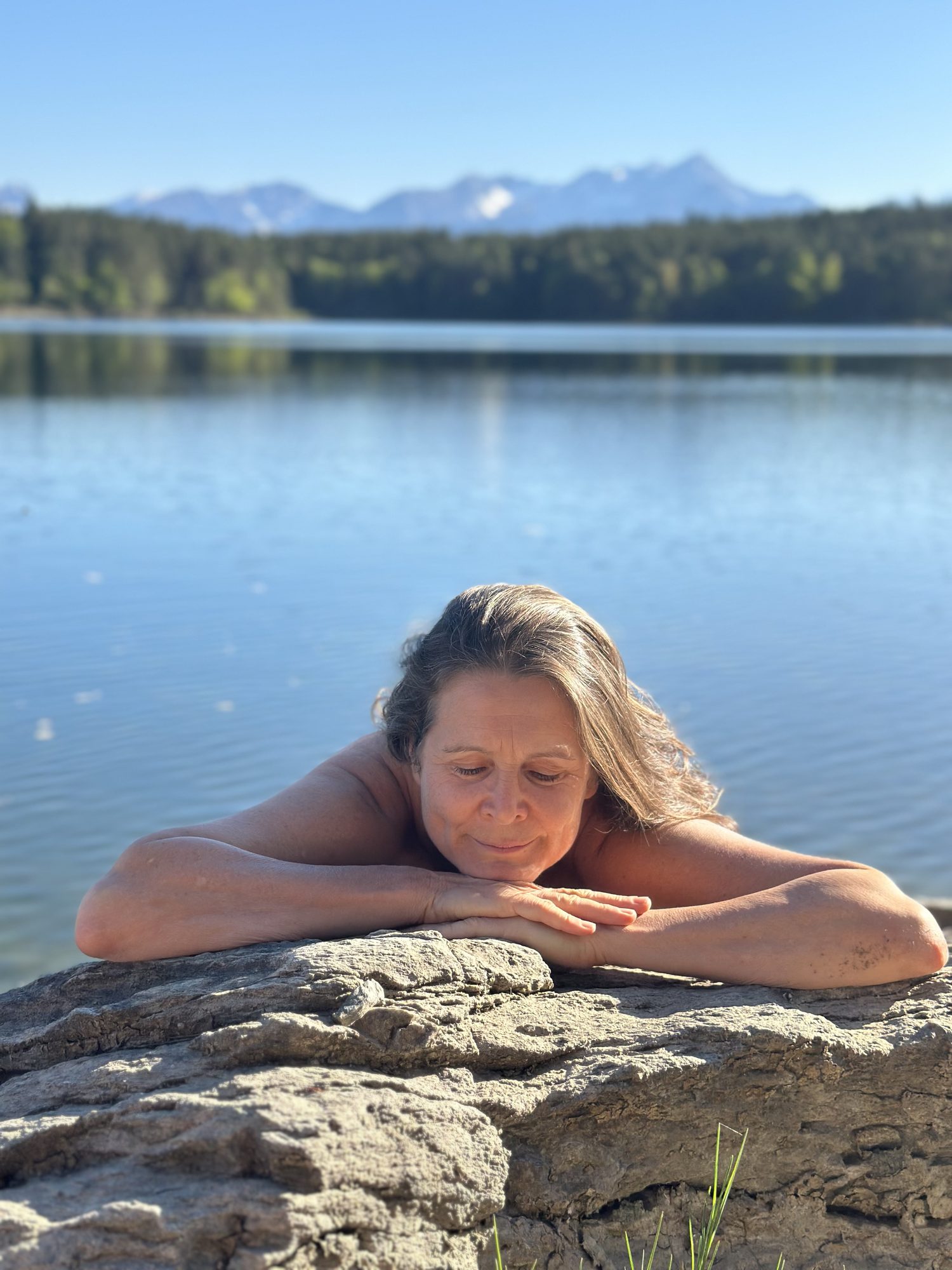 Christina mit geschlossenen Augen, die Arme auf einem Felsen am See