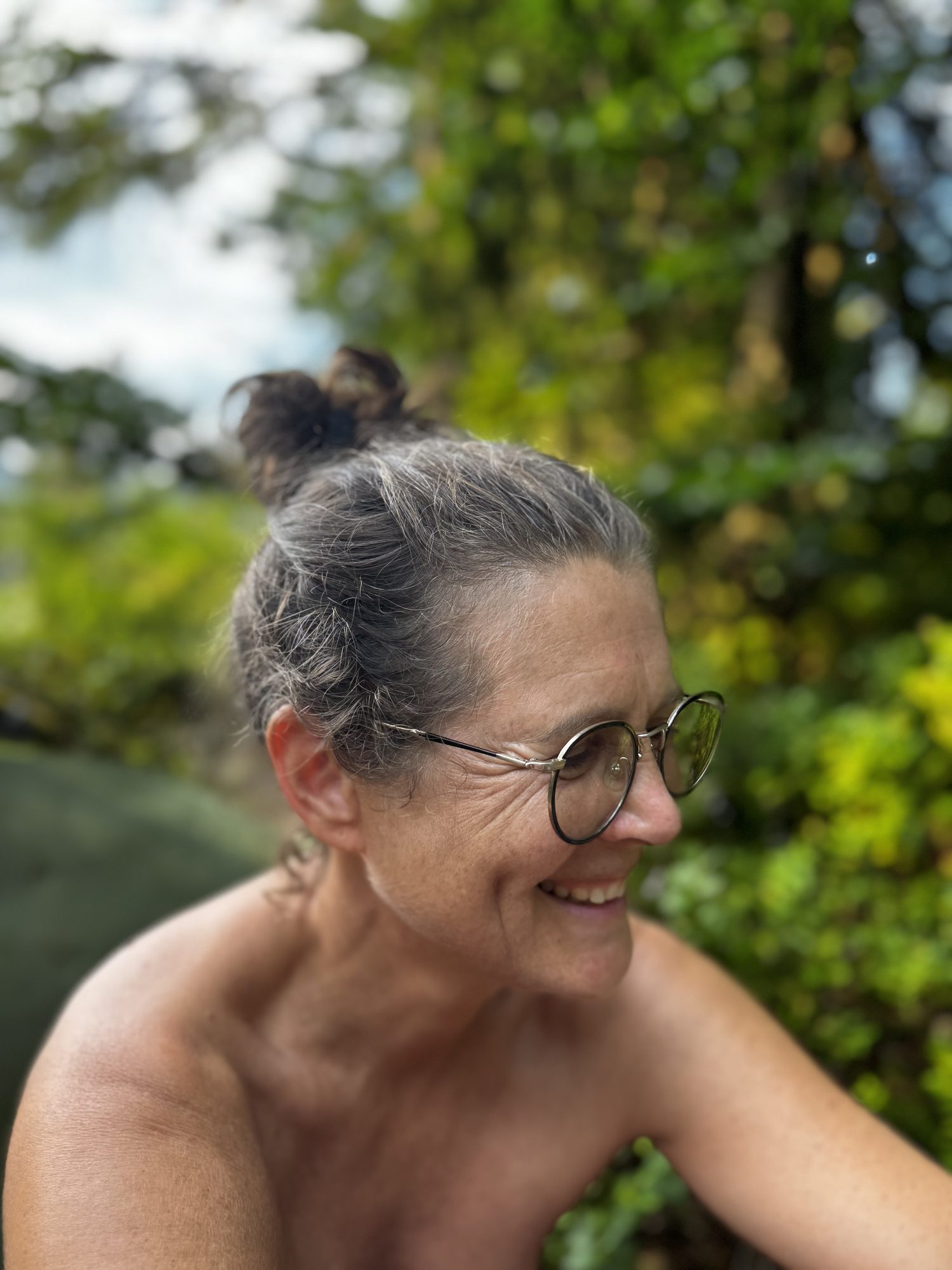 Christina laughing, shoulders bare, in the green of the forest