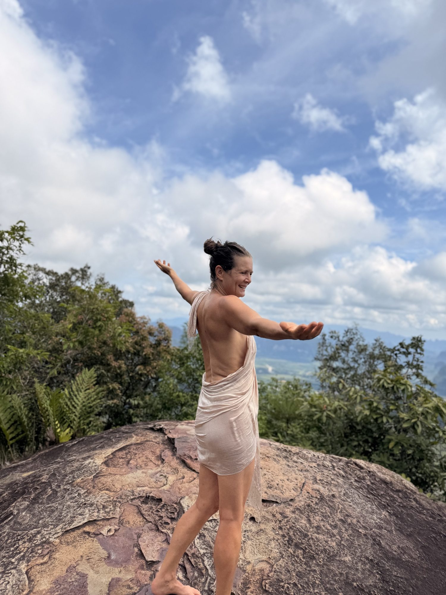 Christina standing on a rocky summit with open arms, wrapped in a cloth
